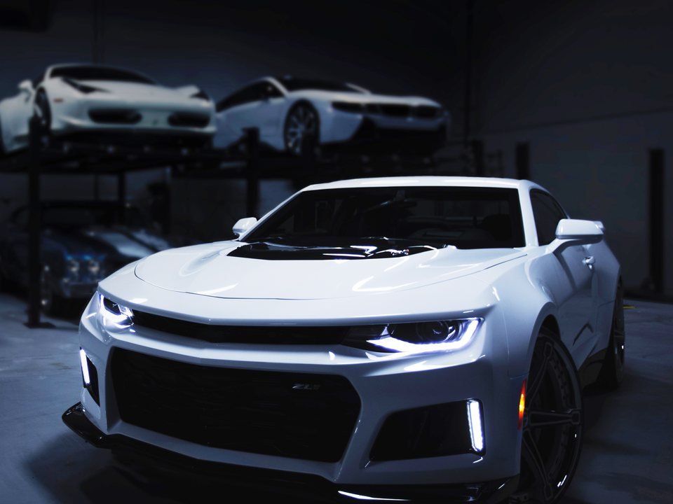 White sports car parked in a clean, enclosed workshop bay ready for preparation