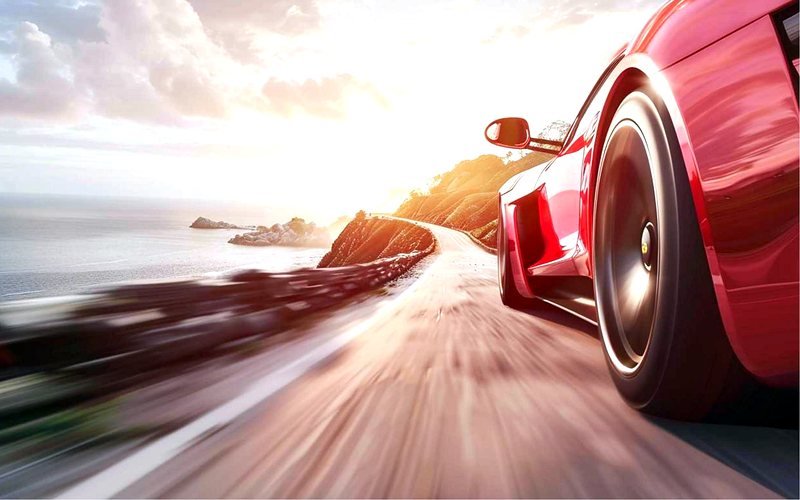 Red sports car on a coastal road in low, hot sunlight