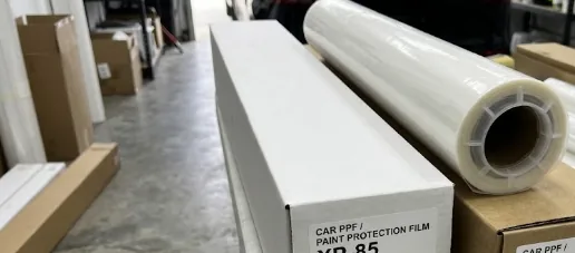 Carton of car paint protection film next to a clear PPF roll