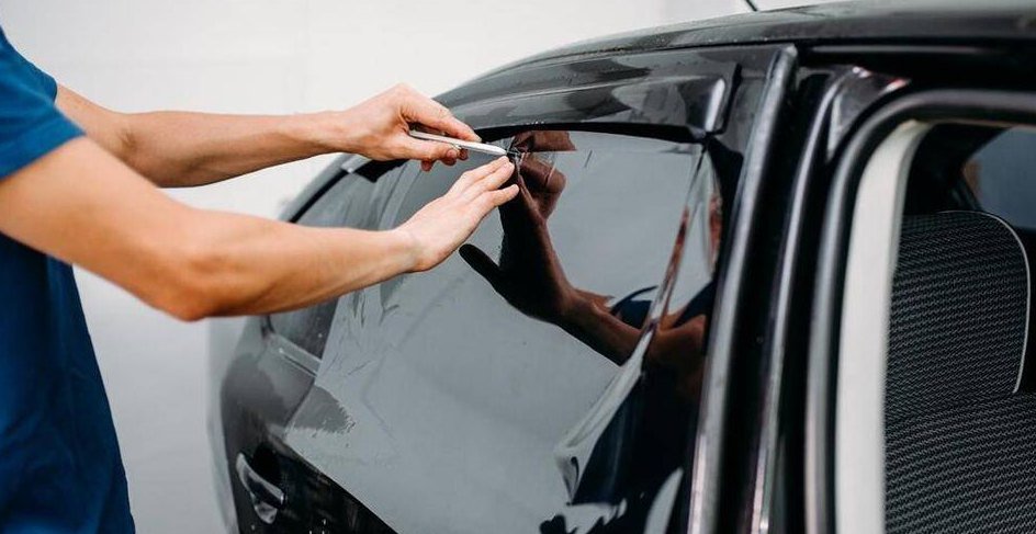 Tint shop installer applying dark dyed window film to a car side window